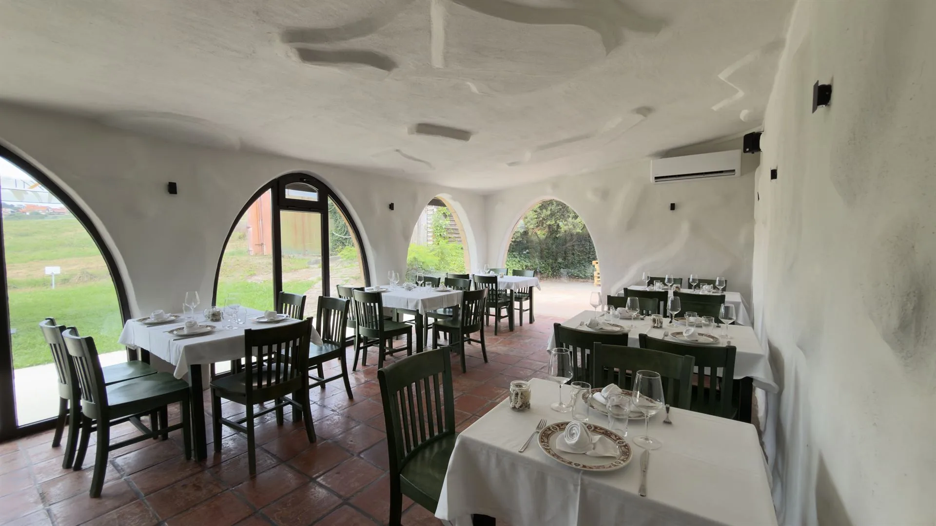 Comedor de Las Teresitas con ventanales en arco, mesas vestidas de blanco y sillas verdes