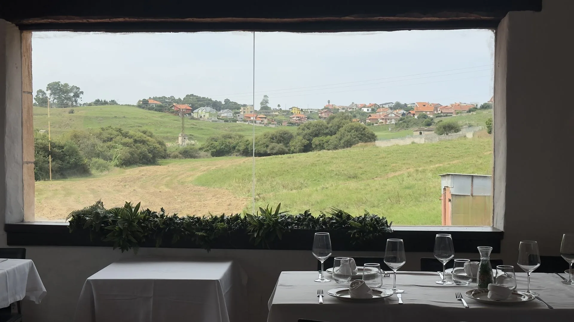 Mesa preparada junto al ventanal del comedor, con la campiña de Suances al fondo