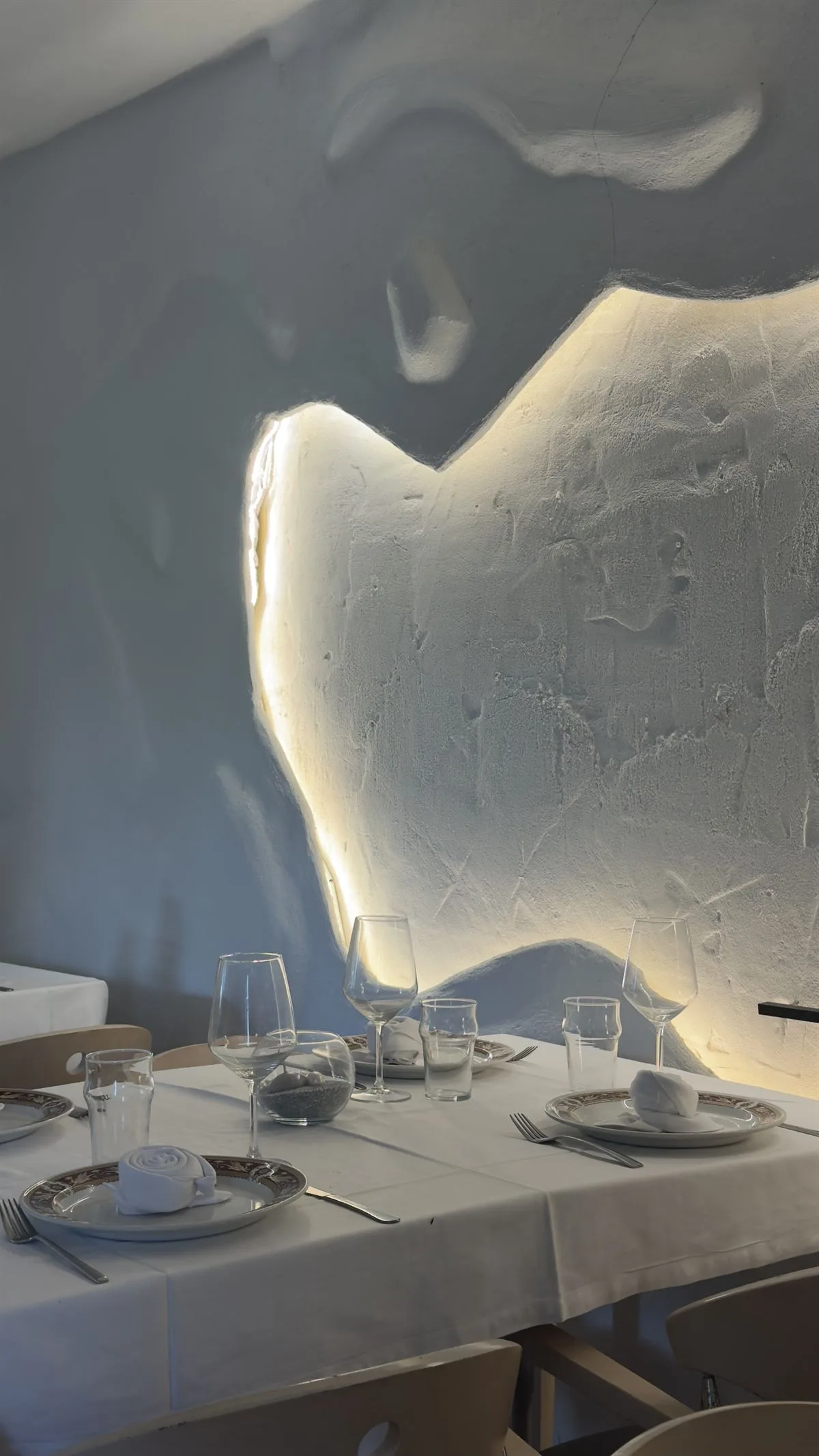 Mesa preparada junto al muro esculpido e iluminado del comedor
